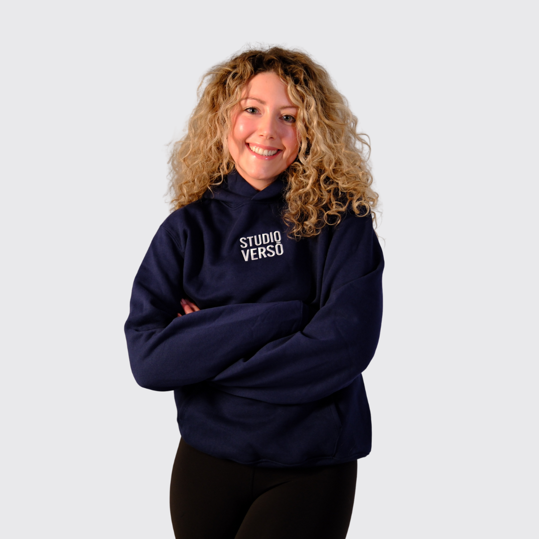 Person wearing a navy hoodie with embroidered Studio VERSŌ stacked logo